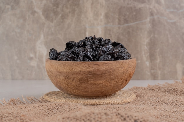 Dry black plums in a wooden cup on a piece of burlap.