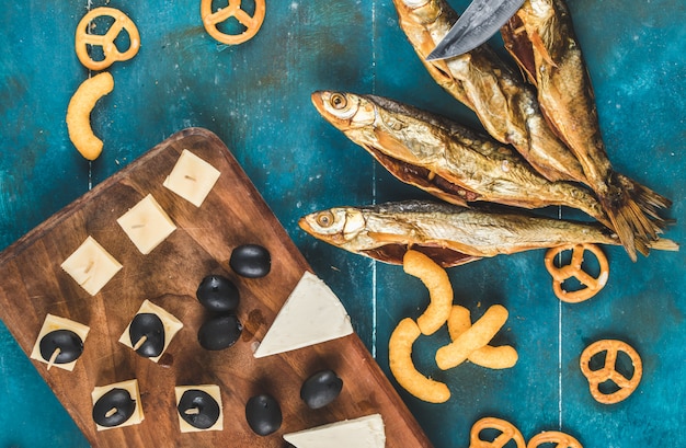 Free photo dry fish snack with cheese, olive and crackers on the blue table, on a wooden board