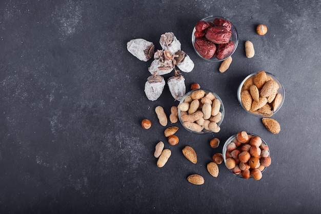 Dry nuts and fruits in a glass and wooden cups on grey surface, top view. 