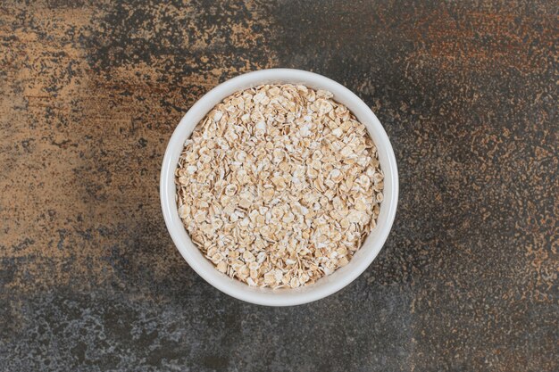 Dry oat flakes in white bowl. 