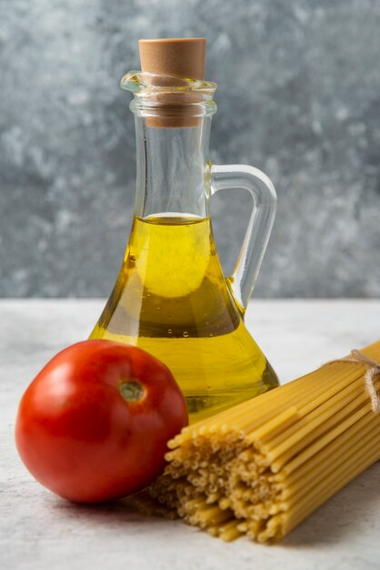 Dry spaghetti, bottle of olive oil and tomato on white table. 