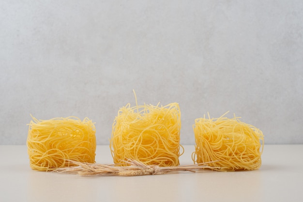 Free photo dry spaghetti nests on white surface with wheat