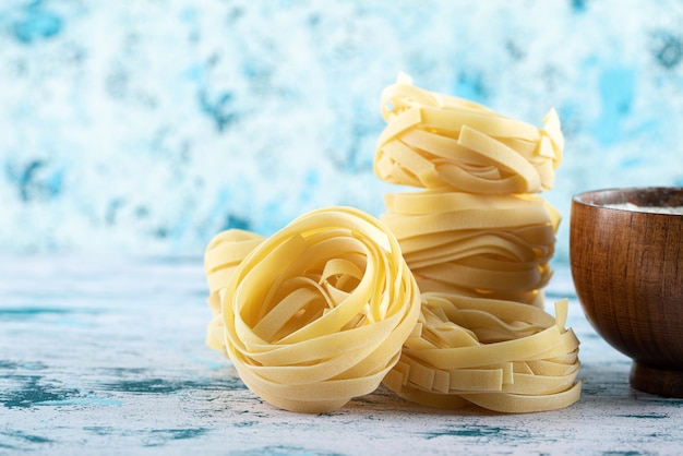 Free photo dry tagliatelle nests and bowl of flour on colorful surface.