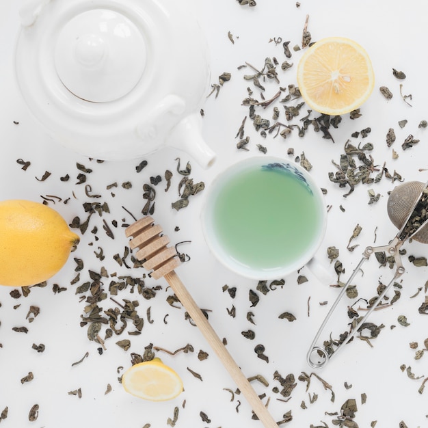 Free photo dry tea leaves; tea strainer; lemon; fresh green tea; and teapot on white backdrop