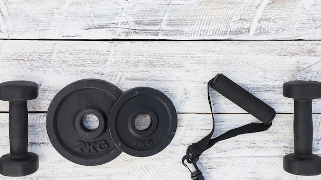 Free Photo dumbbells; weight plates and fitness strap on white wooden textured background