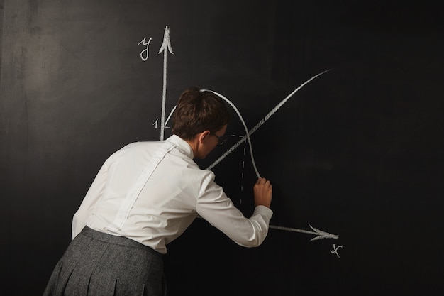 Free photo during a maths class teacher in conservative clothes draws graphs on the blackboard with white chalk