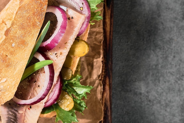 Free photo dutch sandwich with herring, pickled cucumbers and red onions on a paper lining. ingredients on a cutting board. layout on the table, copy space