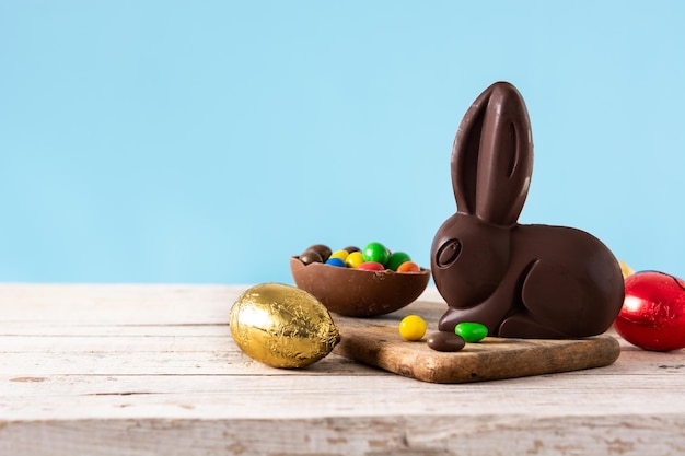 Easter chocolate bunny and colorful eggs on wooden table and blue background