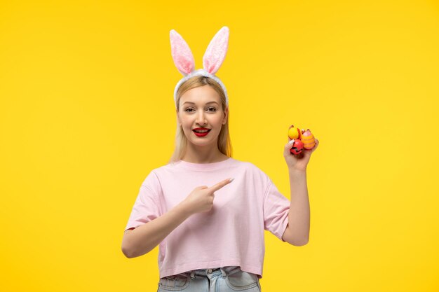 Easter cute young blonde girl wearing pink bunny ears happily smiling and holding easter eggs