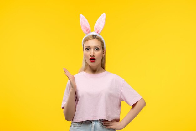 Easter cute young blonde girl wearing pink bunny ears surprised waving hands