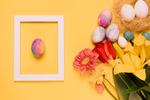 Free photo easter egg white border frame with fresh flowers and eggs nest on yellow background