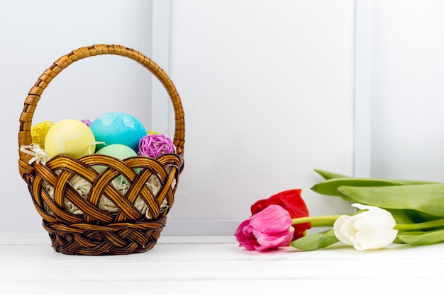 Free photo easter eggs in basket with tulips and blank frame on table