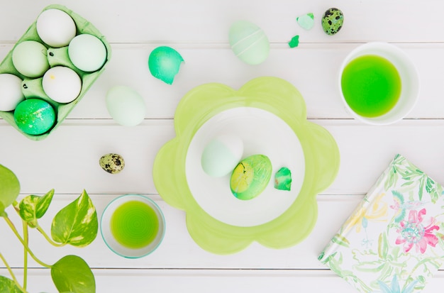 Easter eggs in container near plate, napkin and cup with dye liquid