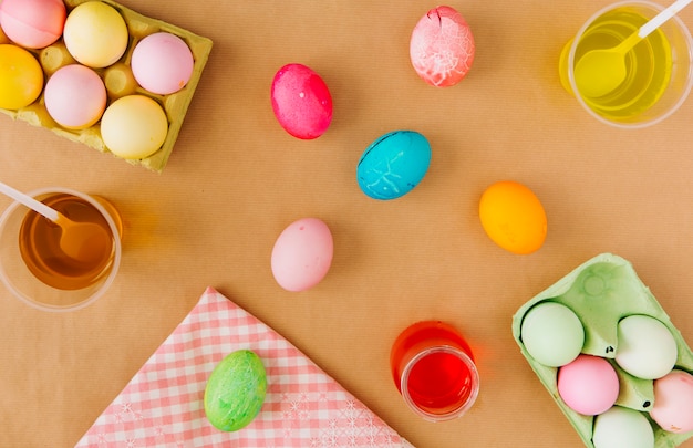 Easter eggs in containers near cups with colourful dye liquid and napkin