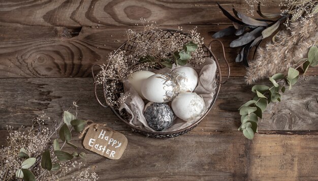 Easter eggs in a decorative basket with dried flowers on a wooden table. Happy Easter concept.