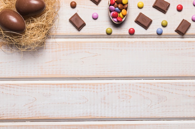 Easter eggs nest; chocolates and gems on wooden desk with space for writing the text