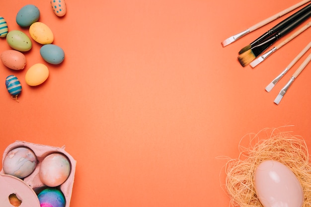 Free photo easter eggs; paint brushes; egg nest on the corner of the orange background