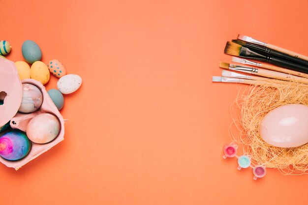 Easter eggs; paint brushes; egg nest on the corner of the orange background