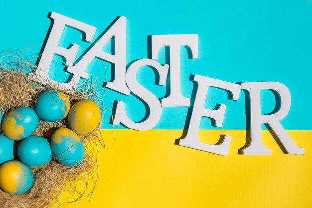 Easter inscription with colourful eggs with hay on bright table