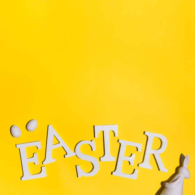 Free photo easter inscription with eggs and rabbit on table