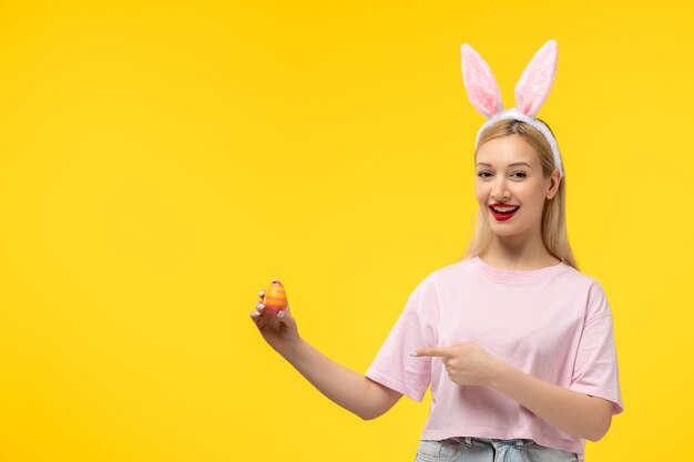 Easter lovely blonde adorable girl with pink bunny ears and red lipstick pointing at easter egg