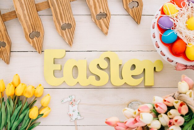 Easter text with fence; rabbit prop; tulips and colorful easter eggs on cakestand on desk