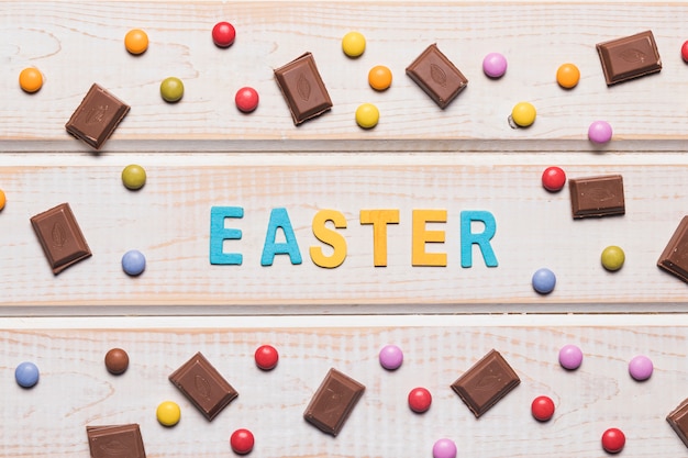 Easter word surrounded with multicolored gems and chocolate pieces on wooden table