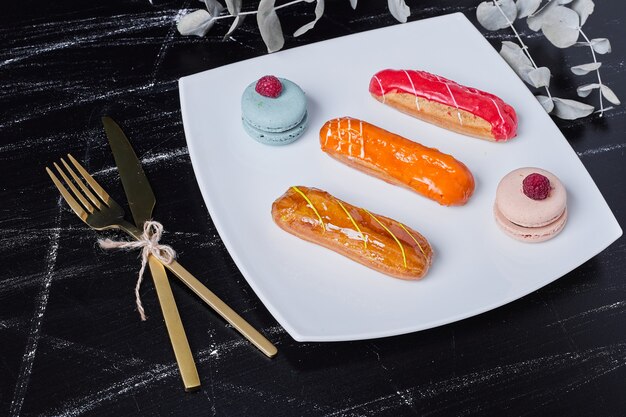 Free photo eclairs with colorful syrups in a white platter.