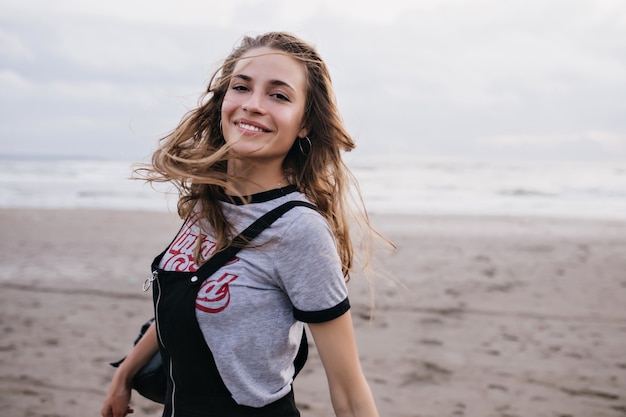 Ecstatic brown-haired girl jumping at beach in cloudy summer day. Photo of attractive white female model posing on nature.