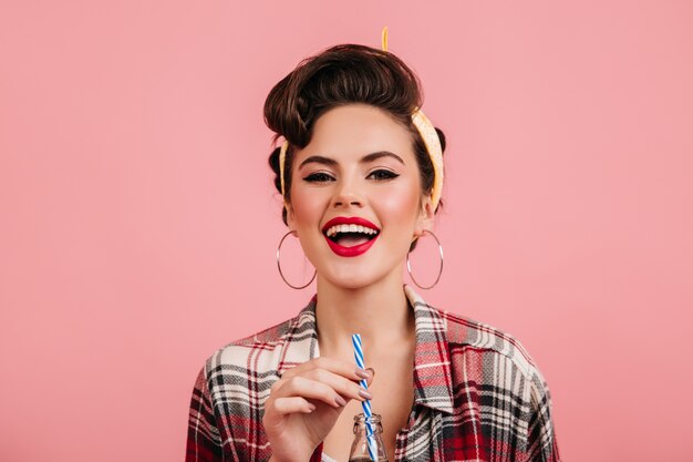 Ecstatic brunette girl drinking beverage. Studio shot of elegant pinup woman isolated on pink background.