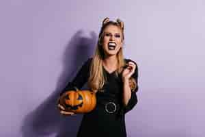 Free photo ecstatic long-haired woman holding halloween pumpkin and laughing.  photo of emotional vampire girl in black dress.