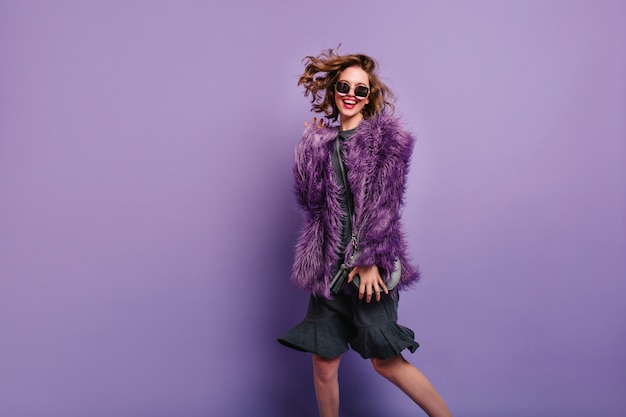 Ecstatic woman in dress and fluffy jacket dancing with laugh