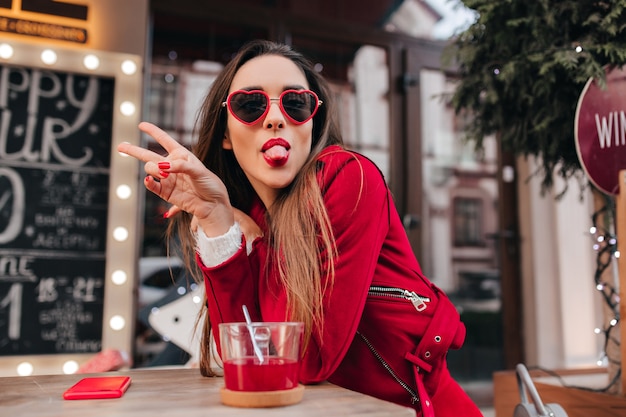 Free photo ecstatic young female model in red glasses posing with tongue out