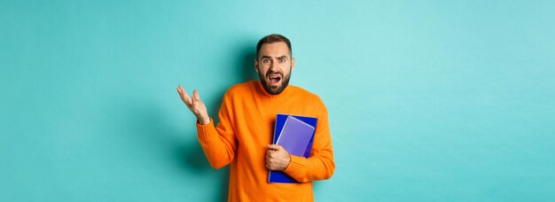 Education confused and disappointed man arguing holding notebooks and complaining standing over ligh