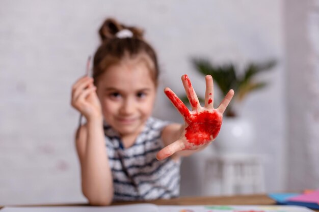 Education, school, art and painting concept - smiling little student girl showing painted hands at school. Paint for drawing