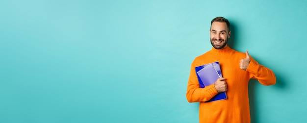 Free photo education smiling bearded man holding notebooks and smiling going on courses showing thumbsup in app