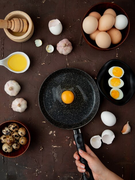 Free photo egg, garlic with butter and egg yolk in frying pan on maroon table