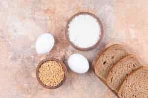 Free photo egg, grain, flour and bread in a wooden plate, on the marble.