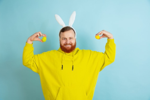 Free photo egg hunt coming. caucasian man as an easter bunny with bright casual clothes on blue studio background.