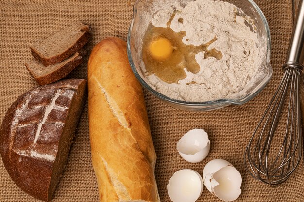 Egg yolk on the flour. Eggshells, baguette and rye bread slices and hand mixer on a piece of burlap. Top view.