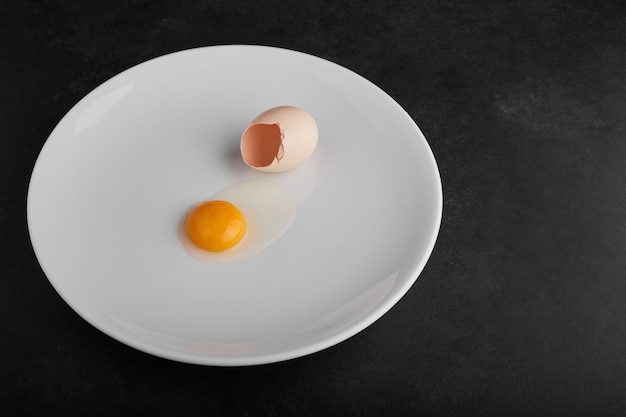 Free photo egg yolk in a white plate with eggshell around.