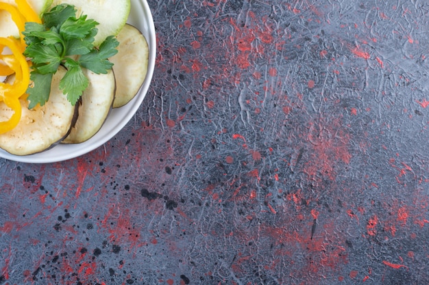 Eggplant and bell pepper slices with a small parsley bundle on a platter on black table.