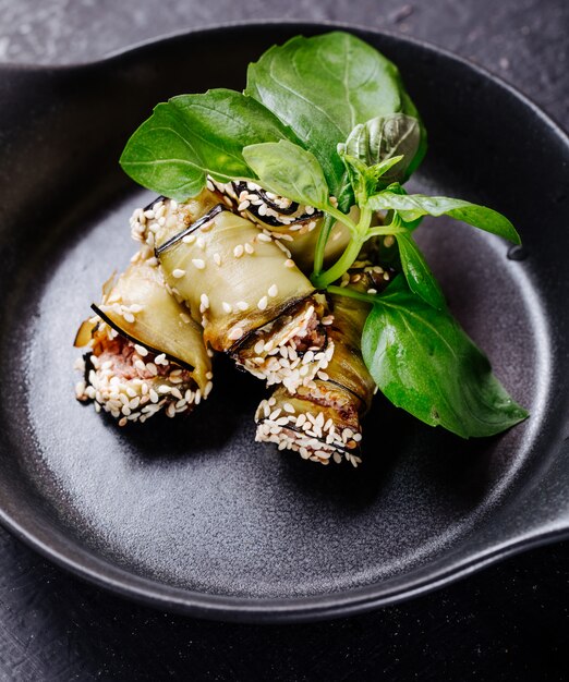 Eggplant rolls with basilic leaves inside black pan.