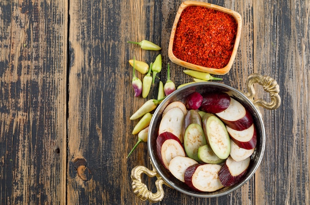 Eggplant slices in a pan with spice, peppers flat lay on a wooden