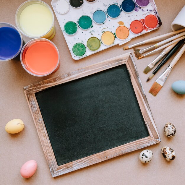 Eggs and blackboard on table with paints