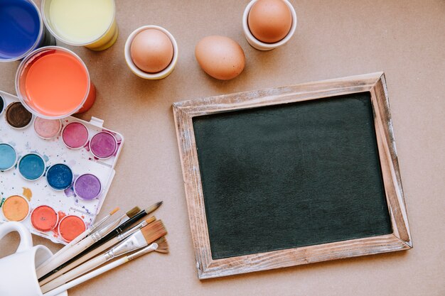 Eggs and blackboard on table with paints