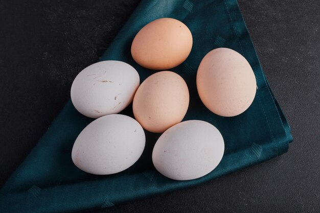 Eggs on a green tablecloth on black surface, top view. 