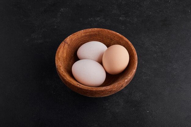 Eggs in a wooden cup on black space. 