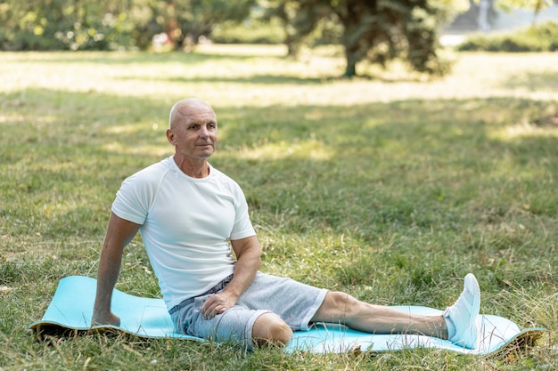 Elder man stretching on yoga mat in nature