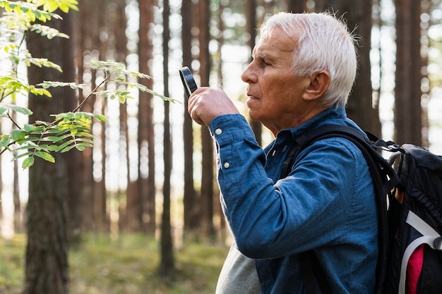 Elder man using magnifying glass while exploring nature with backpack